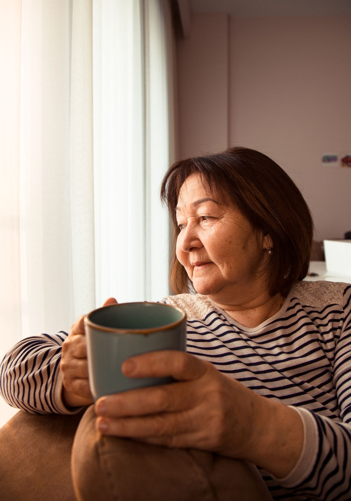 Oudere vrouw geniet zelfstandig thuis van een kop koffie bij het raam